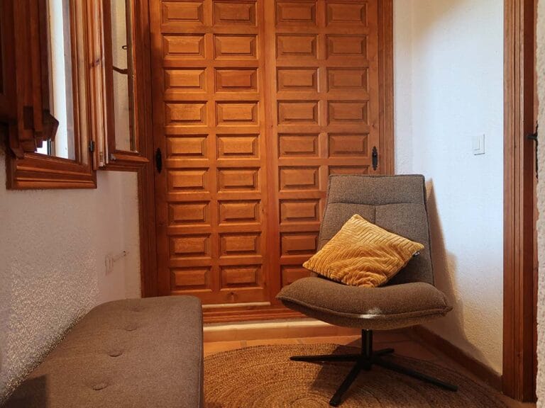 Detail van kamer 'Alcalali' met moderne fauteuil, zitbankje en houten luiken.