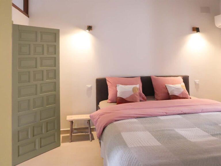 Sfeervolle slaapkamer met opgemaakt tweepersoonsbed en roze accenten bij Casa Llibertat.
