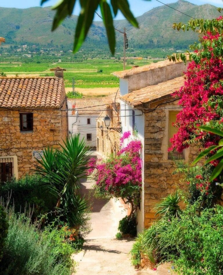 Charmant straatbeeld in Llíber met traditionele natuurstenen gevels, houten luiken en kleurrijke bloemen.