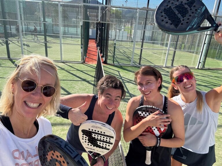 Cuatro mujeres sonrientes con raquetas de pádel se toman un selfie en la pista de pádel durante su viaje deportivo en grupo a Casa Llibertat.